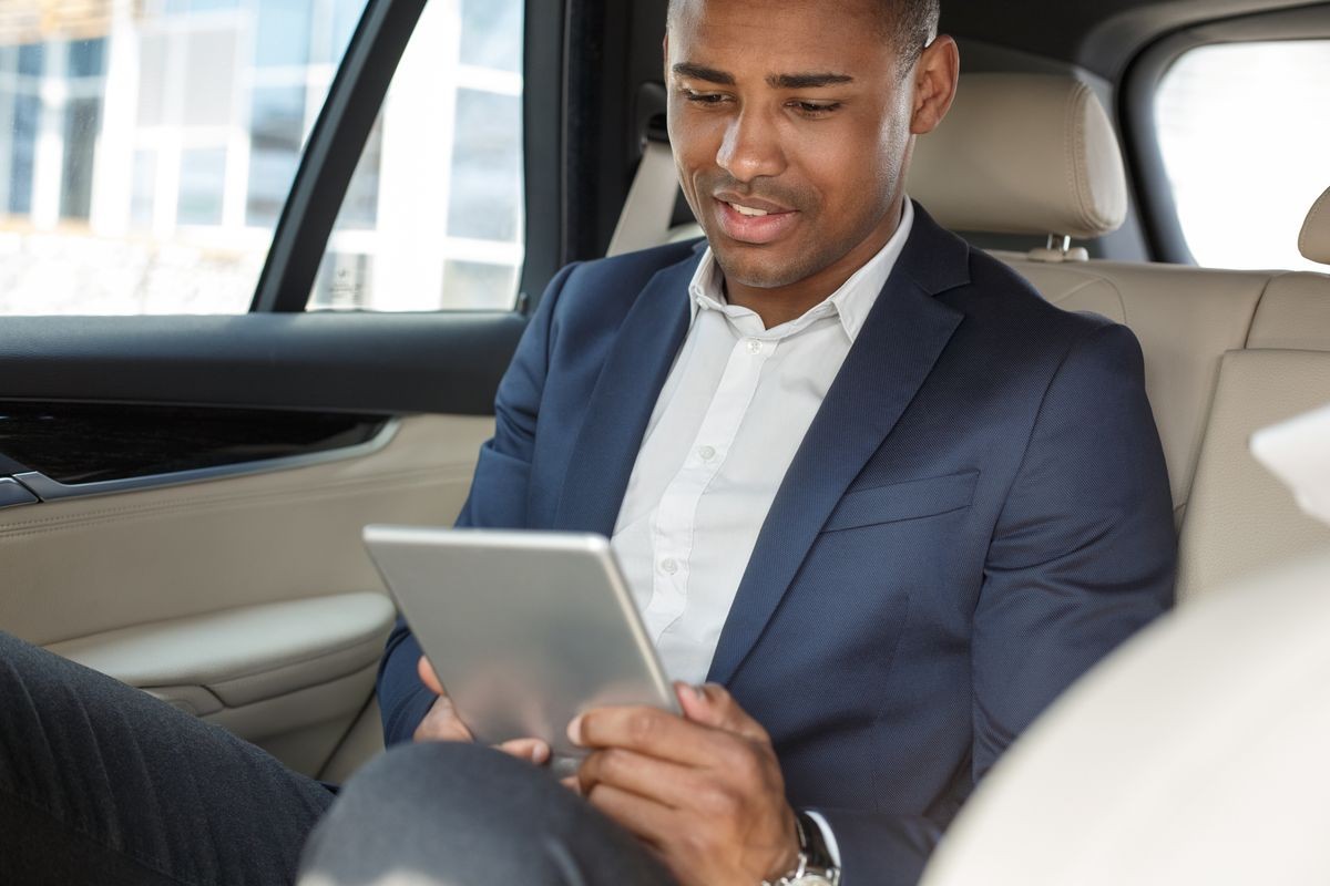 Young businessman sitting on the back seat in the car watching video online smiling happy